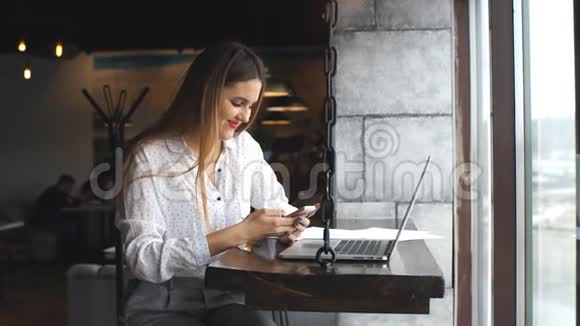 微笑的女商人在她的笔记本电脑上打字使用智能手机视频的预览图