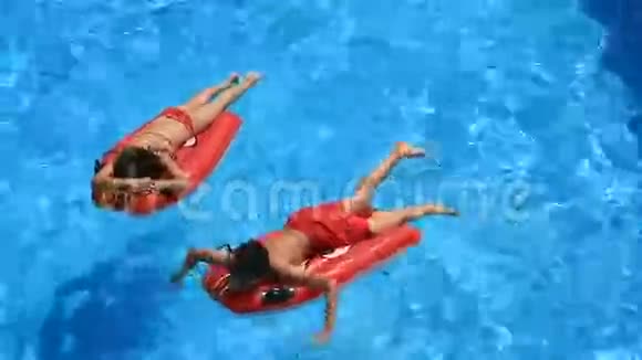 孩子们一个男孩和一个女孩漂浮在游泳池里的充气床垫上从上面看视频的预览图