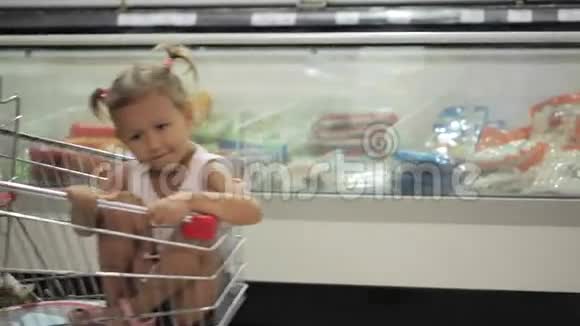 有趣的小女孩坐在超市的购物车里视频的预览图