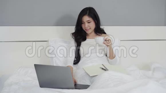 女人喝着一杯咖啡在床上用笔记本电脑视频的预览图