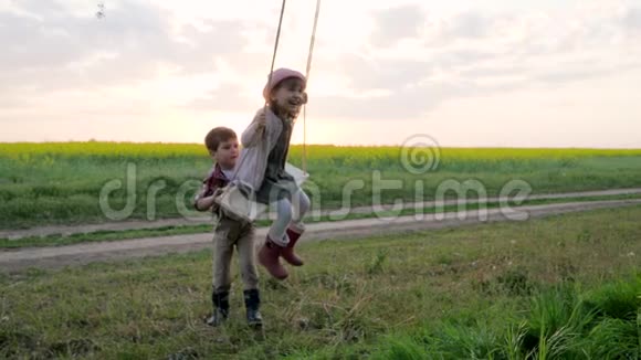 两个孩子骑着孩子们骑着秋千小女孩和男孩在树上旋转微笑着一家人玩得很开心视频的预览图