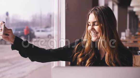 时尚的年轻女性坐在咖啡馆里用她的智能手机自拍视频的预览图