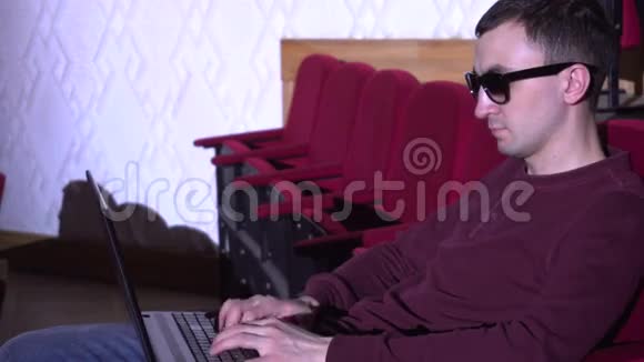 戴墨镜的年轻人用笔记本电脑在音乐厅打字视频的预览图