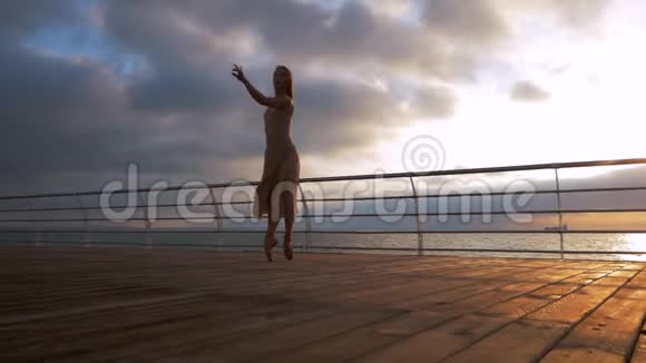 在日出或日落时穿着米色丝质连衣裙和海堤上的尖角跳舞秘书长的信视频的预览图
