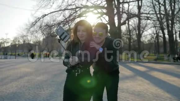 时尚男女孩在公园散步为社交网络拍照小玩意在自拍棒情侣在手机拍照电话视频的预览图