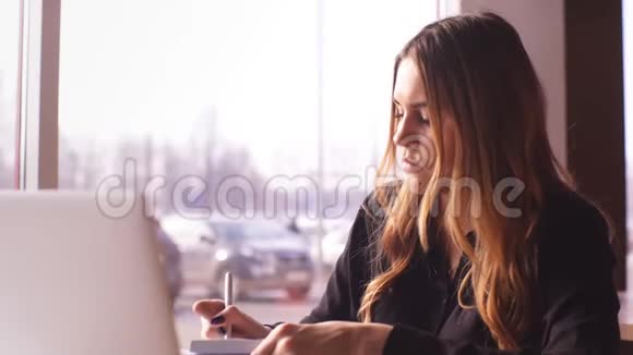 严肃的女商人穿着黑色衬衫在笔记本电脑上工作在笔记本上记笔记视频的预览图