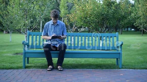 在公园里坐在长凳上写字板的男人视频的预览图