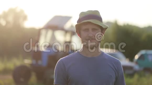 戴帽子的年轻农民站在有机农场的田野上微笑的肖像视频的预览图