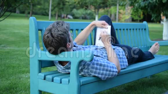 苗条的男人躺在长凳上写着记事本视频的预览图