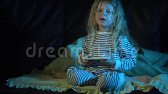 一个晚上穿着条纹睡衣的小女孩在房间里用智能手机视频的预览图