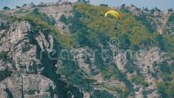 橙色条纹的黄色滑翔伞在灰色大岩石的背景下在美丽的山区飞行视频的预览图