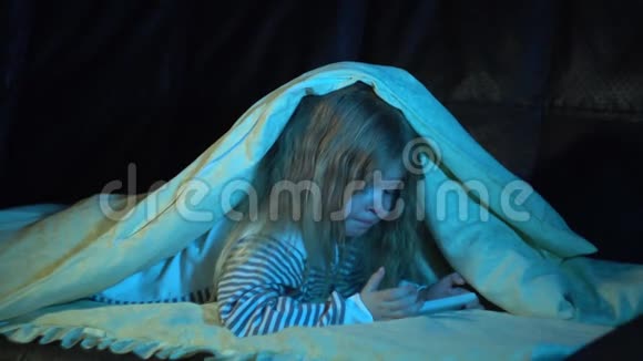 一个晚上穿着条纹睡衣的小女孩在房间里用智能手机视频的预览图