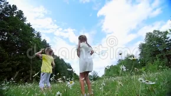 在绿色的洋甘菊草坪上女孩孩子们打羽毛球他们跑跳到处乱跑他们玩得很开心夏季视频的预览图