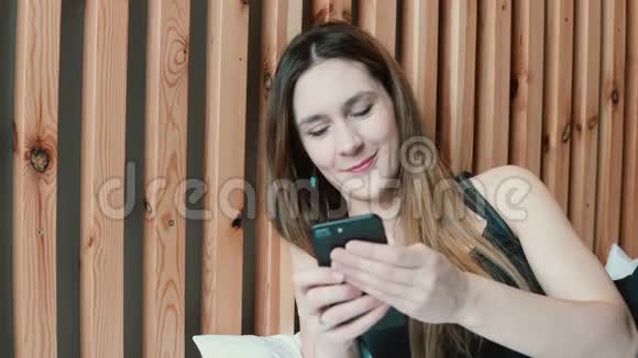 幸福的年轻女人用智能手机躺在家里的沙发上微笑女孩在客厅里打电话发短信视频的预览图