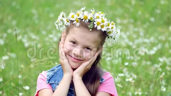 在一片洋甘菊的草坪上一个戴着雏菊花圈的甜美女孩微笑着双手贴在脸颊上视频的预览图