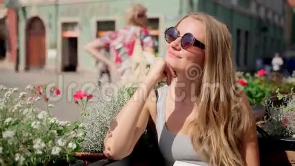 年轻漂亮的金发女孩的户外肖像戴着复古圆太阳镜独自坐在老城咖啡馆里等待一个人视频的预览图