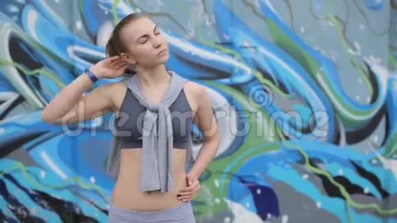 在涂鸦背景下年轻的运动女孩在锻炼前做头发视频的预览图