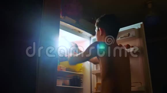 小男孩晚上从冰箱里吃饥饿和饕餮青少年男孩晚上看冰箱饕餮视频的预览图