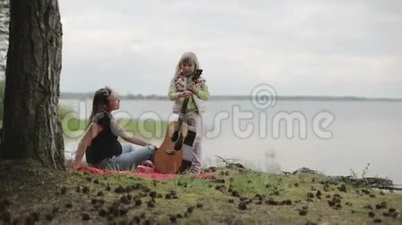 在多云的天气里女儿在湖岸为母亲弹吉他视频的预览图