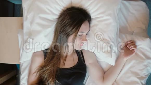新鲜快乐的女人躺在床上女人早上醒来微笑着黑发长发女孩下床视频的预览图