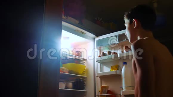 小男孩晚上从冰箱里吃饥饿和饕餮青少年男孩晚上看冰箱的生活方式视频的预览图