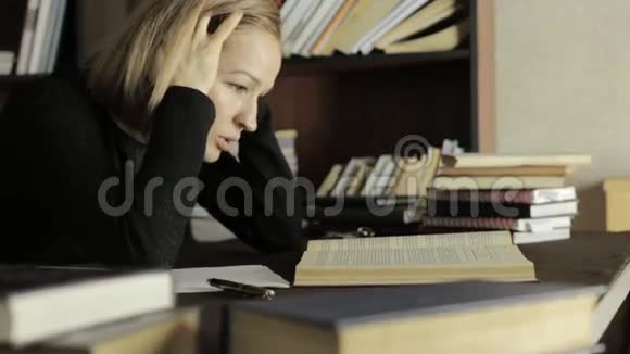 疲惫的学生在大学里在图书馆学习坐在书桌前抓着她的头的女学生视频的预览图