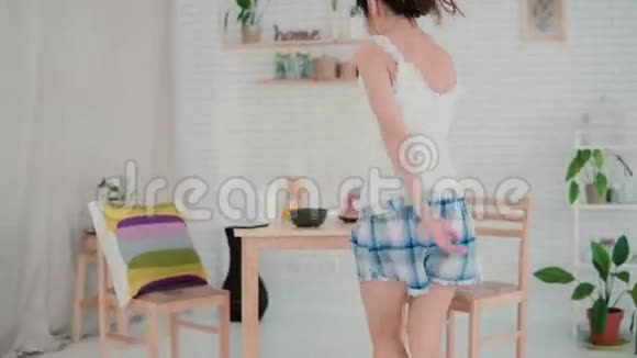 早上在厨房跳舞的漂亮年轻女人穿睡衣的布鲁内特女孩在家吃早餐视频的预览图