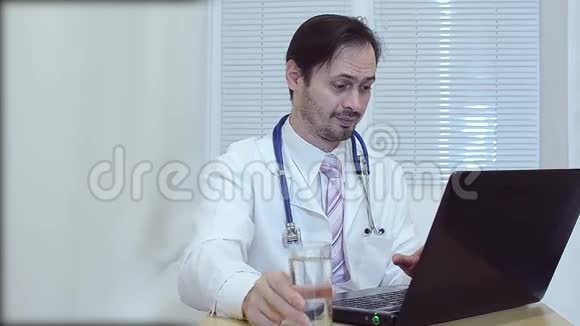医生喝了一杯水医生在办公室为一台笔记本电脑工作视频的预览图