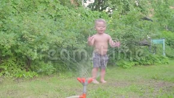 快乐的小男孩在外面玩夏天的花园里有喷水器慢动作视频的预览图