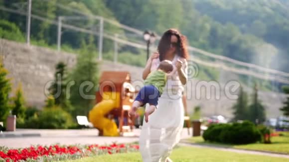 妈妈在和宝宝玩妈妈在公园里缓慢地亲吻和旋转一个小儿子视频的预览图