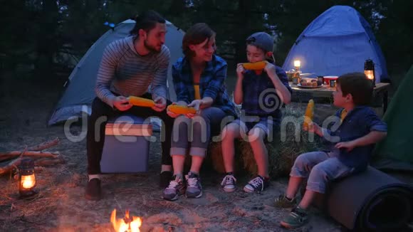 在大自然中野餐一家人用盐吃玉米去野营妈妈爸爸和儿子从外面吃新鲜的黄色玉米视频的预览图