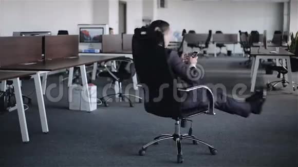 一位手里拿着手机的年轻商人正坐在大办公室的扶手椅上转过身视频的预览图