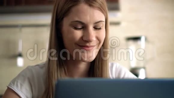 美丽迷人的休闲年轻女子坐在厨房里通过信使与朋友交谈视频的预览图
