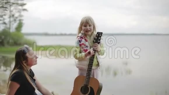 慢动作美丽的小女孩在湖边的森林里弹吉他给妈妈唱歌视频的预览图