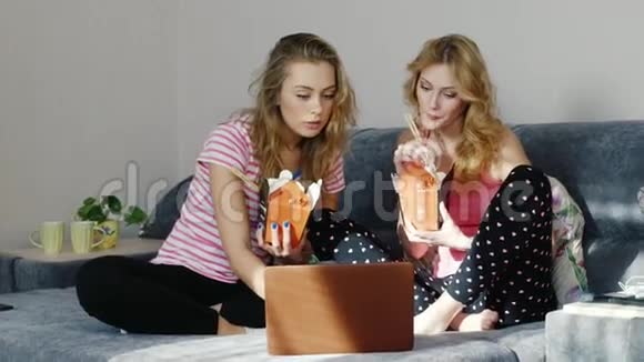 两个年轻的女人从纸袋里吃快餐用木筷子他们附近有一台笔记本电脑网上订餐视频的预览图
