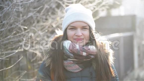 外面寒冷阳光下平静美丽的女孩的肖像戴着白帽和格子围巾的布鲁内特在微笑视频的预览图