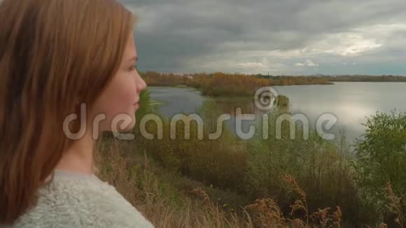 年轻的白种人金发女郎指着秋湖的岸边视频的预览图