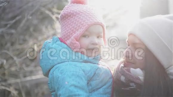 平静的母亲抱着可爱的小女儿清晨在公园里享受寒冷的阳光天气妇女和女孩视频的预览图