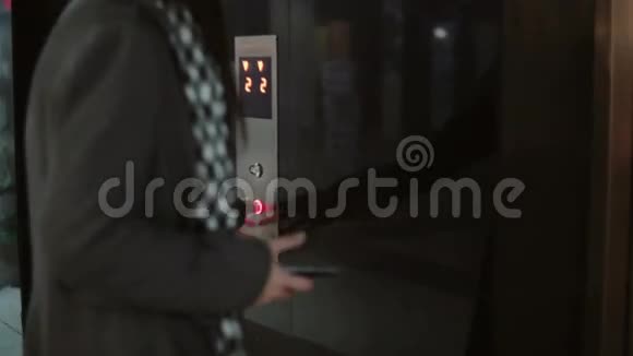 女人按下电梯里的按钮等待女性站在办公室使用智能手机触摸屏幕视频的预览图