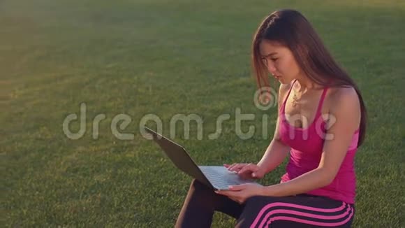 在绿草上用笔记本电脑工作的亚洲女人有魅力的女人用笔记本视频的预览图