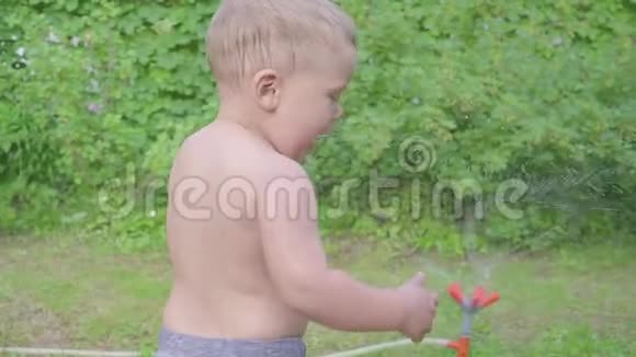 可爱的小男孩在外面玩夏天的花园里有喷水器慢动作视频的预览图