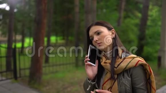 漂亮的年轻女孩在她的手机上说话户外夏日公园里一个轻松的年轻女子谈话的肖像视频的预览图