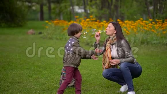 漂亮的年轻妈妈和她一个非常可爱的小儿子在夏天快乐地在户外吹泡泡慢动作视频的预览图