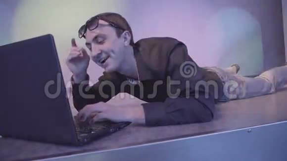 带着笔记本电脑的好斗的年轻人躺在夜总会的地板上视频的预览图