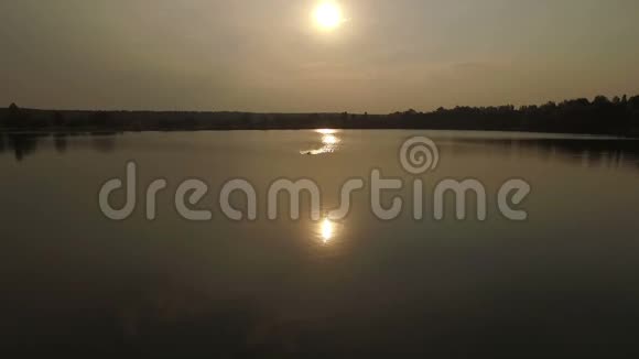日落时分在湖中游泳的金发男子的航拍镜头视频的预览图