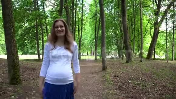 微笑的孕妇独自在公园散步抚摸她的腹部视频的预览图