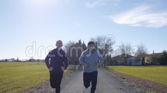 与户外私人教练一起健身2名男子在绿茵场背景下沿着乡间小路慢跑视频的预览图
