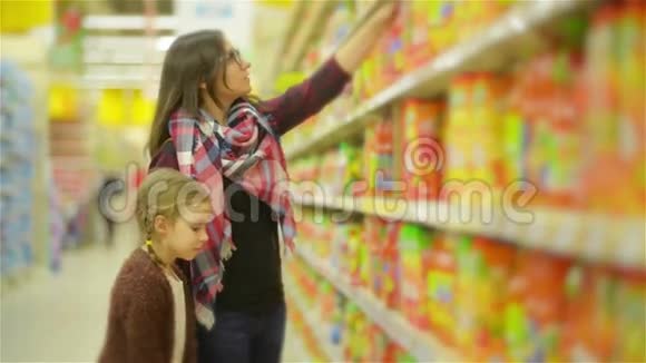 微笑的母亲和她的小女儿在超市购物美丽的女人与可爱的女孩从架子上挑选视频的预览图