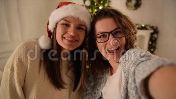 两个美丽的女孩在圣诞树背景上玩自拍布鲁内特修女使用智能手机视频的预览图