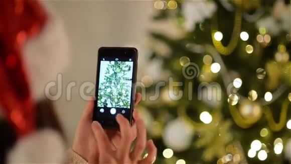 圣诞帽里的女士用智能手机拍圣诞树圣诞云杉装饰精美视频的预览图